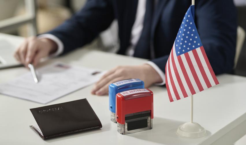 U.S. immigration officer reviewing EB5 visa application paperwork with approval and rejection stamps and a small American flag in focus.