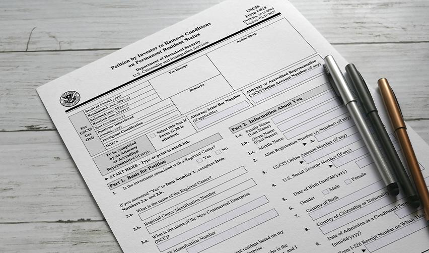 A blank USCIS Form I-829 petition on a wooden desk with pens, representing the process of applying to remove EB5 Green Card conditions.