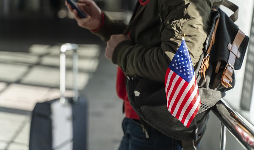 At an airport, a person carries a backpack displaying the U.S. flag, reflecting the uncertainty EB5 investors face when navigating visa restrictions under new travel policies and Supreme Court-backed executive authority.