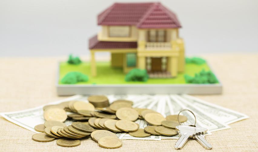 A miniature model house surrounded by U.S. dollar bills, coins, and house keys, representing real estate financing and tax considerations for EB5 investors.