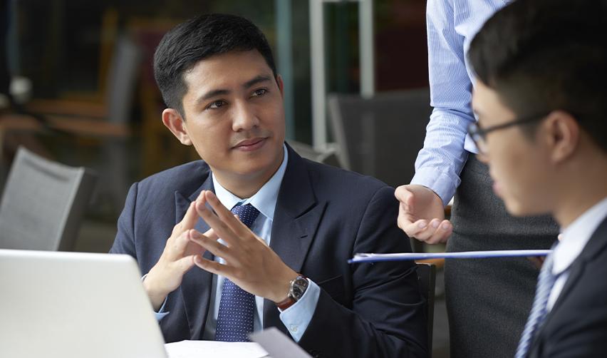A professional man in a suit engaged in a thoughtful conversation with colleagues, illustrating tech investors planning their entrepreneurial journey through the EB5 program with EB5AN's help.