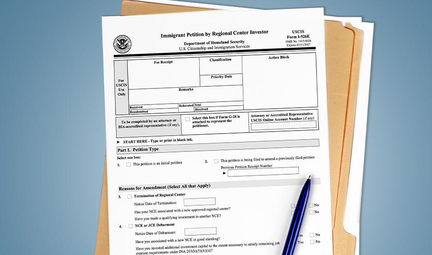 Close-up of USCIS Form I-526E for EB5 regional center investors, resting on a file folder with a blue pen, symbolizing the first step in the EB5 Green Card process.