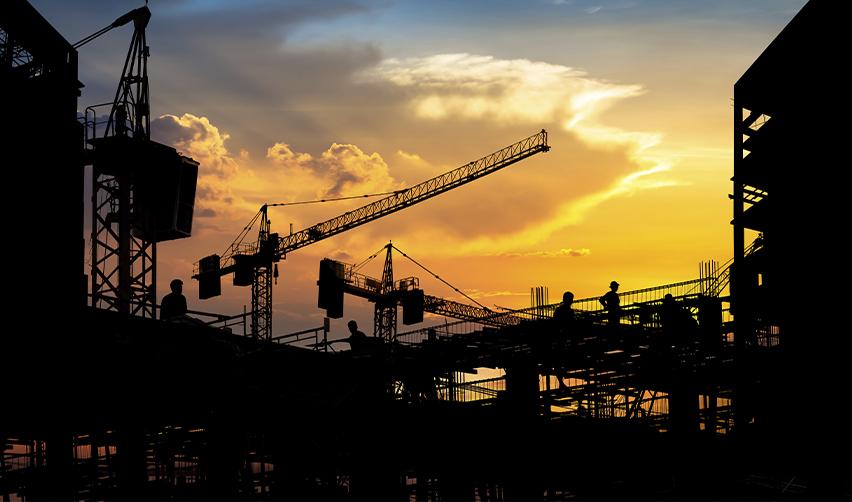 Construction site at sunset with cranes and silhouetted workers, symbolizing EB5 job creation through real estate development in a job-creating entity.