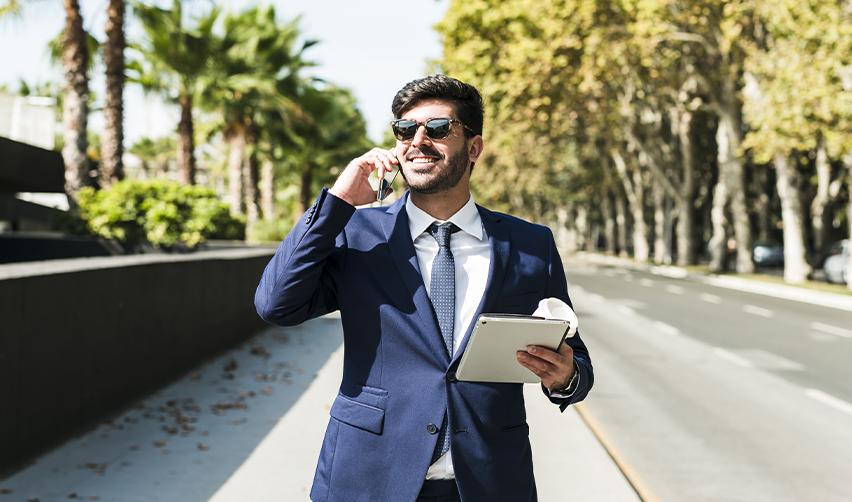A confident businessman in a navy suit walks while talking on the phone and holding a tablet, symbolizing professional life in the U.S. made possible through EB5 concurrent filing and EAD.