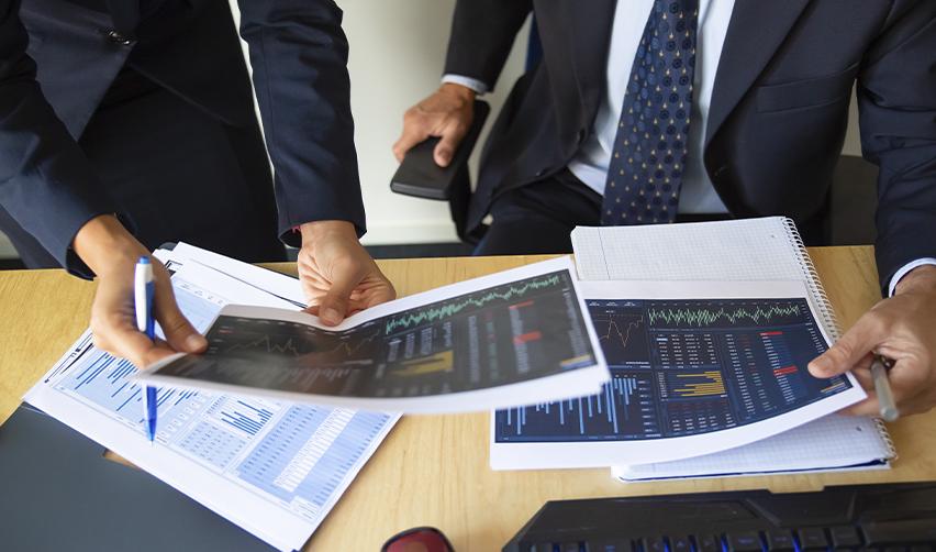 Two professionals in suits reviewing printed financial reports and job creation charts, representing the importance of regular project reporting and transparency in EB5 investments.