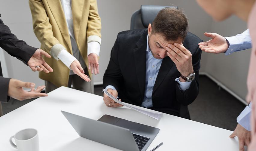 A stressed businessman at a desk surrounded by people demanding answers, symbolizing the pressure EB5 investors may face if a regional center shuts down unexpectedly.