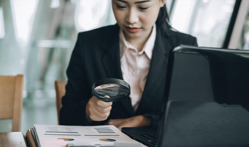 Professional woman reviewing documents with a magnifying glass, representing due diligence in EB5 investment decision-making.