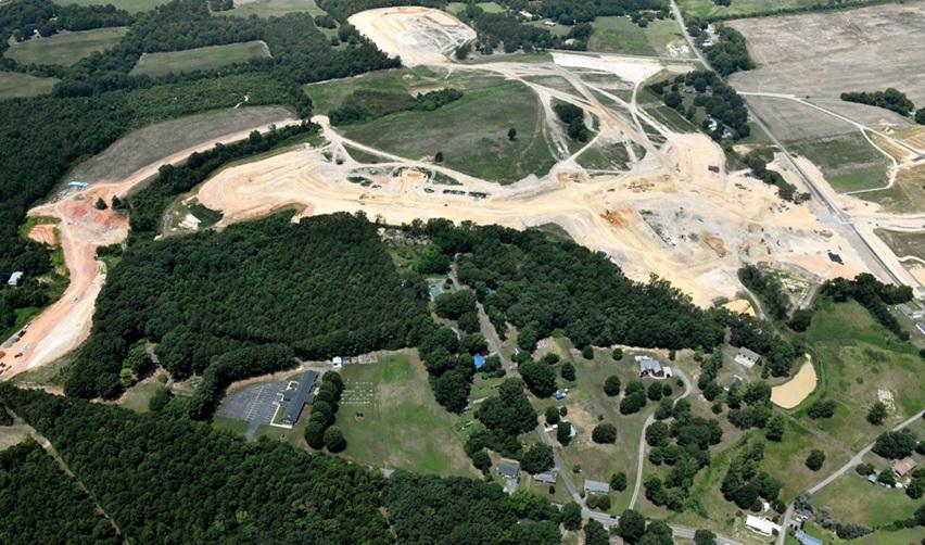 Aerial view of Rocky River EB5 community construction site in Locust, North Carolina, showing extensive land grading, cleared plots, and surrounding wooded areas.