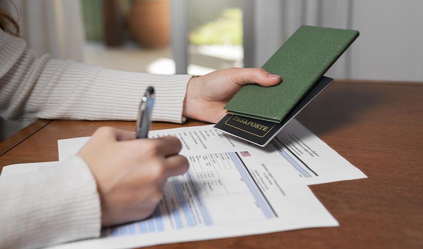 Hands completing a USCIS petition form while holding a passport, representing EB5 investors managing immigration paperwork alongside other visas.