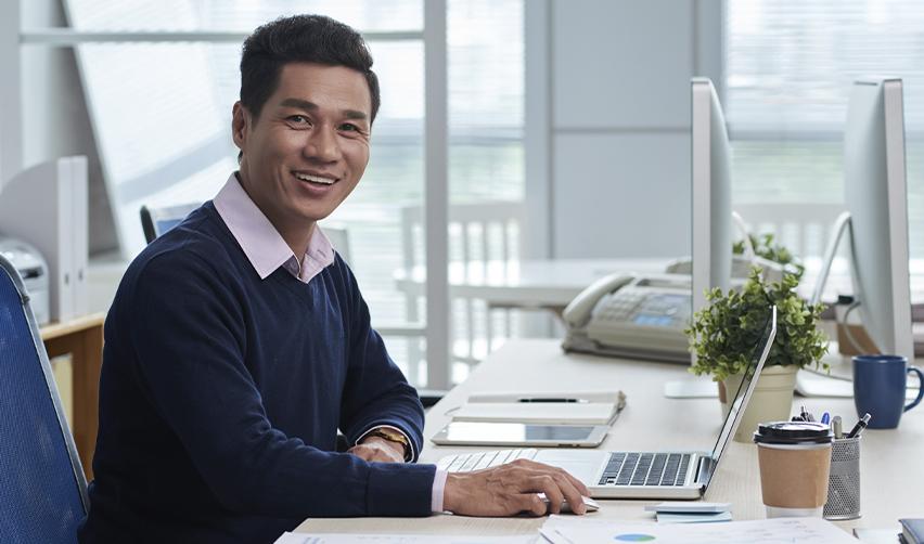 Smiling professional sitting at a desk with a laptop, symbolizing EB5 investors preparing and filing applications while set-aside categories remain current.