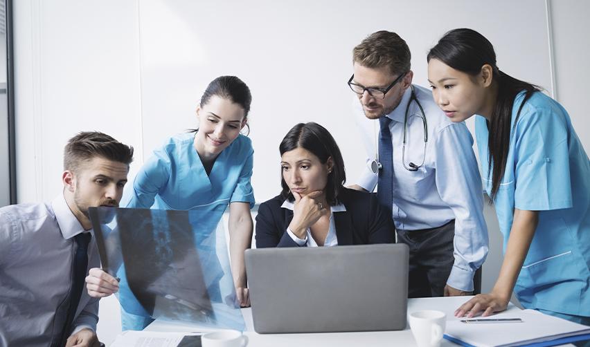 A team of physicians and medical staff reviewing X-rays and data on a laptop in a modern clinical setting, illustrating the collaborative process of U.S. medical residency programs after graduate medical education.