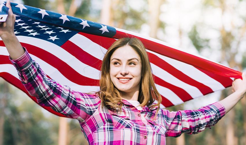 Smiling woman holding an American flag outdoors, representing the freedom and pride of obtaining a U.S. Green Card through EB5.