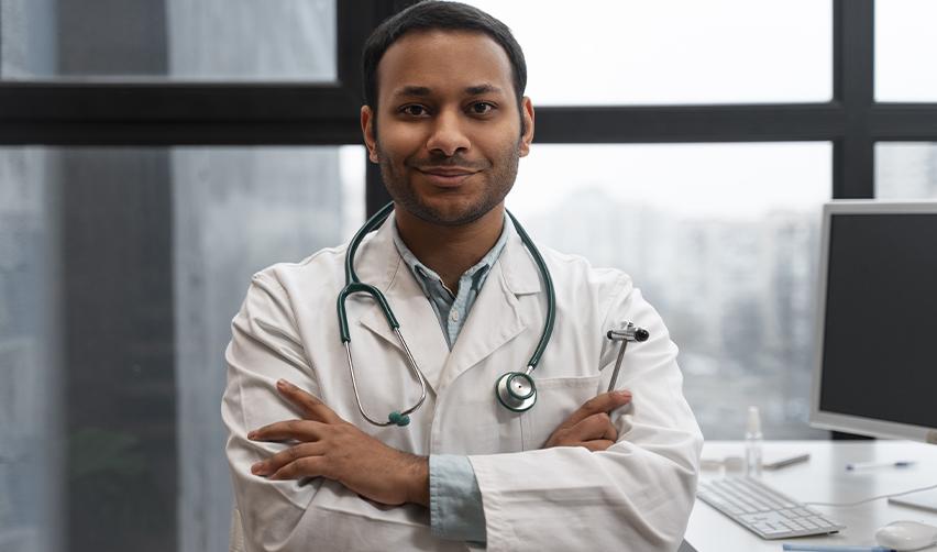 A confident foreign national physician standing with arms crossed in a medical office, representing Indian doctors achieving permanent residency and stability in the United States through the EB5 visa.