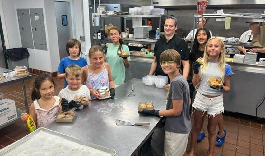 Group of children in Bay Creek’s Tavern kitchen holding homemade cookies during the July 18 Cooking with Chef Linda kids’ workshop.