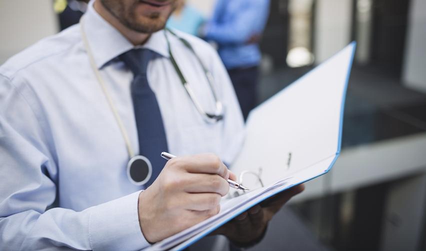 A close-up of a foreign national physician writing notes in a medical file as trained during his graduate medical education from an accredited medical school, reflecting compliance with licensing and documentation requirements in U.S. healthcare practice.