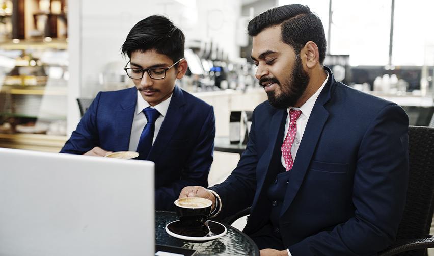 Two Indian professionals in business suits working on a laptop, symbolizing indian microsoft H1B workers exploring EB5 visa investment opportunities.