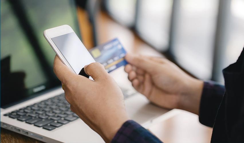 Hands holding a smartphone and credit card above a laptop, symbolizing USCIS’s move to electronic payments for EB5 petitions.