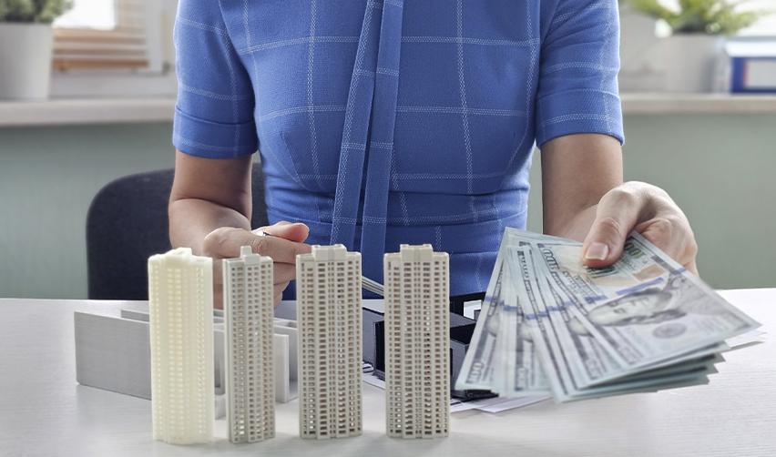 Investor holding U.S. dollar bills beside miniature high-rise models, illustrating EB5 real estate funding and capital investment.