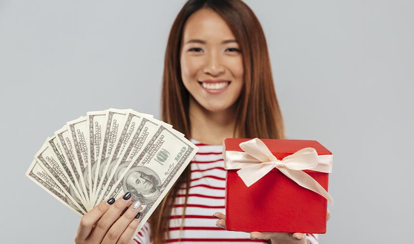 Smiling woman holding U.S. dollars and a gift box, illustrating gifted funds in EB5 visa applications.