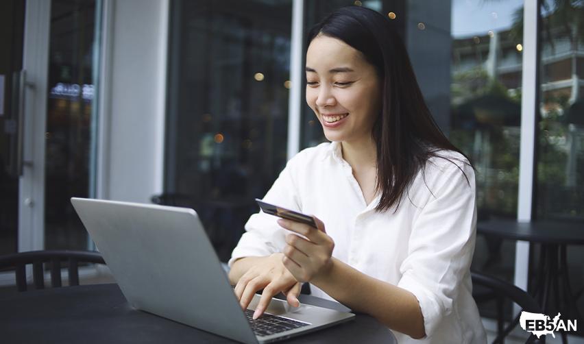 EB5 investor smiling while making a secure online payment with a credit card on her laptop, representing USCIS’s digital payment requirement.