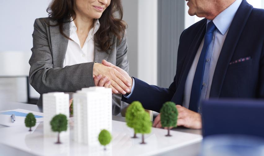 Two professionals shaking hands over real estate models, representing EB5 regional center and developer partnerships.