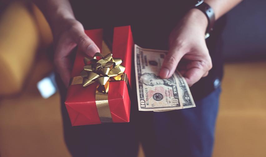 Close-up of hands with a red gift box and U.S. dollars, symbolizing family gifts as EB5 investment funds.