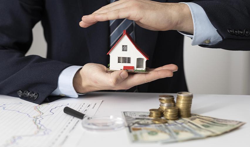 Hands holding a miniature house above coins and U.S. currency, symbolizing security and repayment protections in EB5 investments.