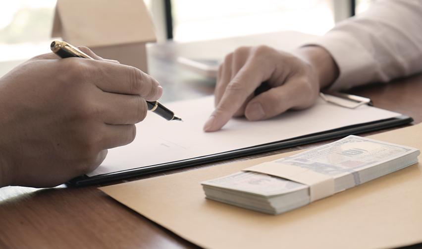 Two people reviewing and signing EB5 investment documents on a desk with a stack of U.S. dollar bills, symbolizing investor filing fees and financial compliance.