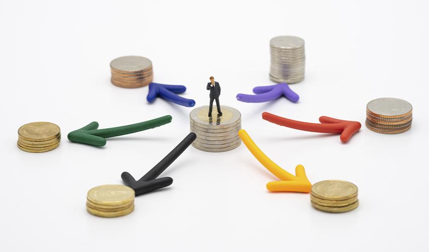 A miniature businessman standing on stacked coins surrounded by colorful arrows, symbolizing how EB5 investments flow through different sectors and create ripple-effect job growth.