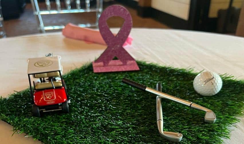 Close-up of Pink Ball Tournament table décor with a pink ribbon, golf-themed accessories, and a miniature golf cart, symbolizing Bay Creek’s support for breast-cancer awareness.