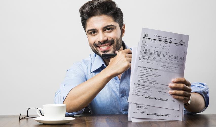 An indian investor smiling while holding EB5 application forms and a cup of coffee, illustrating confidence and independence gained through the EB5 green card.