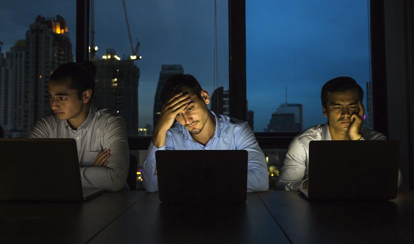 Group of H1B workers sitting at laptops late at night, looking stressed about layoffs and visa uncertainty, highlighting risks compared to EB5 stability.