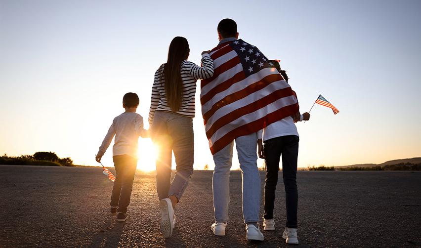 Family walking together with an American flag at sunset, symbolizing EB5 investors achieving U.S. permanent residency and future security.