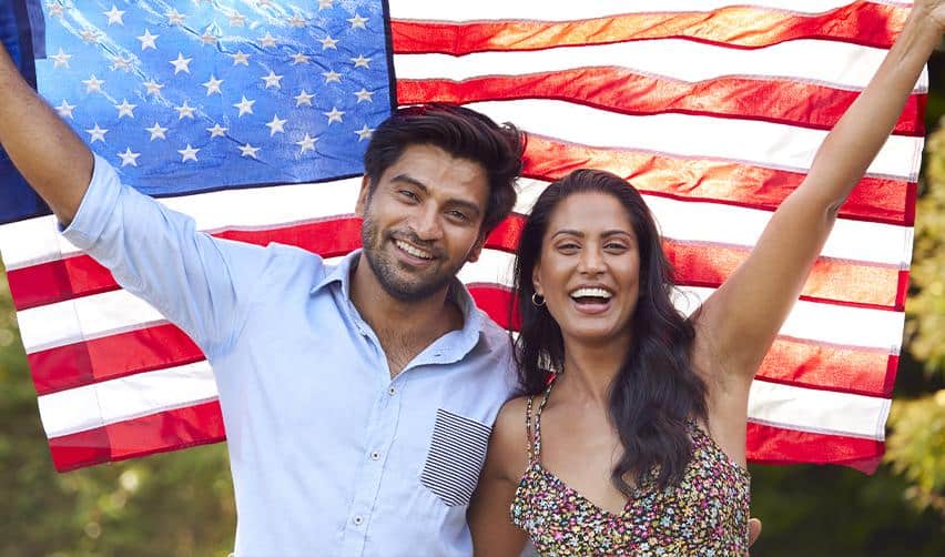 A happy Indian couple celebrating with an American flag outdoors, symbolizing families achieving permanent residency in the U.S. through the EB5 program.