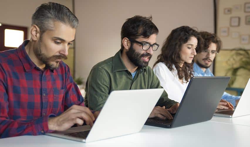 Four tech professionals collaborating on laptops in an office, symbolizing the dependence of Indian H1B workers on employer sponsorship compared with EB5 independence.
