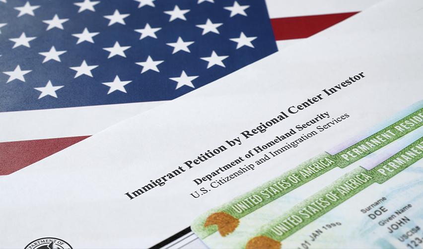 Form I-526E and a U.S. permanent resident card placed over an American flag, representing the EB5 immigration process and the return to lower filing fees.