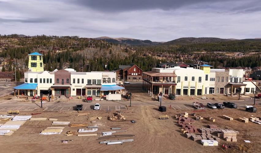 A view of Market Street at Grand Park with commercial buildings under construction, showing exterior cladding, window installation, and surrounding mountain landscape in Colorado.