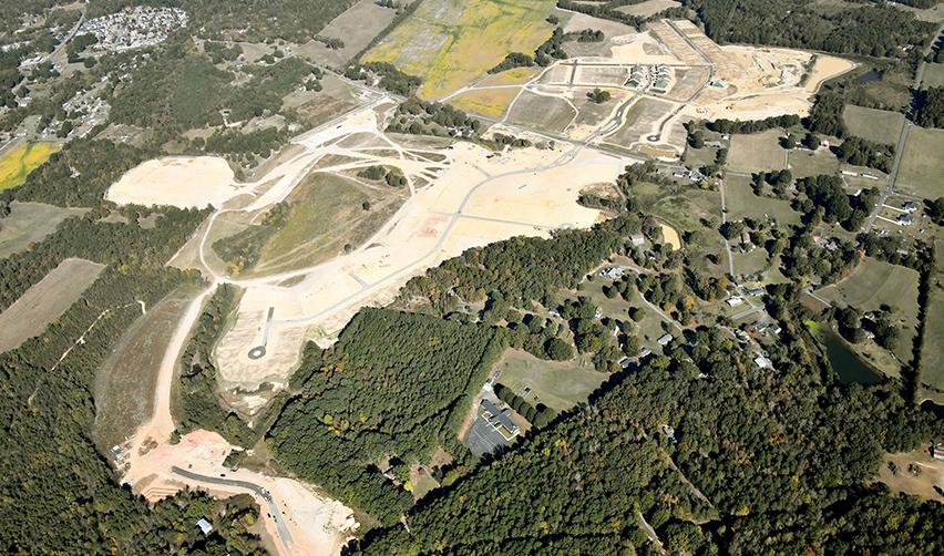 Wide aerial view of the Rocky River EB5 development with active earthwork, new streets, and surrounding wooded areas.
