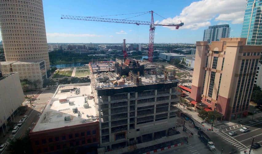 Updated view of ONE Tampa construction site with multiple floors completed, active cranes, and surrounding high-rises illustrating steady progress in the city center.