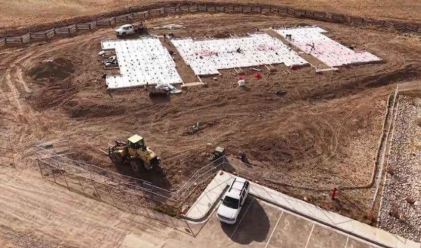 Crews working over insulated foundation panels at Grand Park, with heavy equipment and grading visible as construction advances before winter.