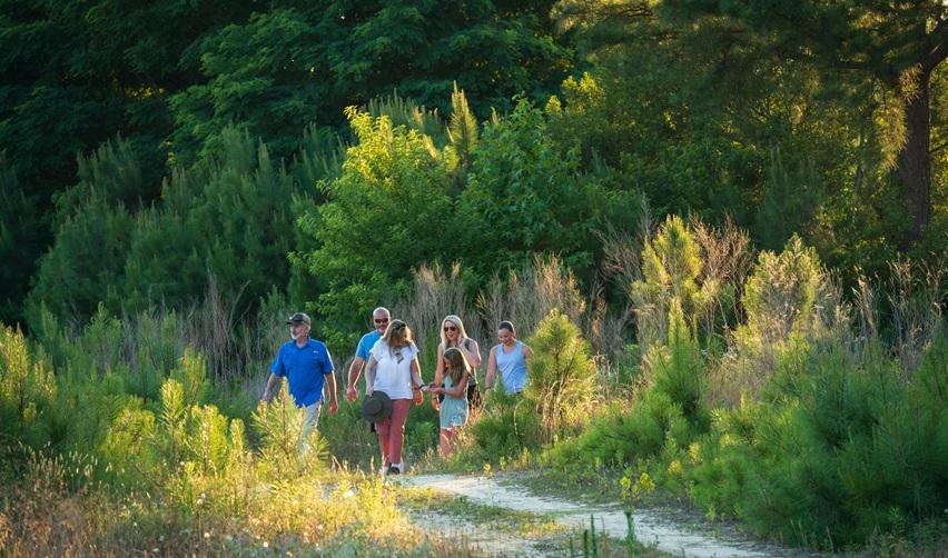 Residents walking through Bay Creek’s nature preserve trails surrounded by native greenery, reflecting the community’s conservation efforts and eco-focused EB5 development model.