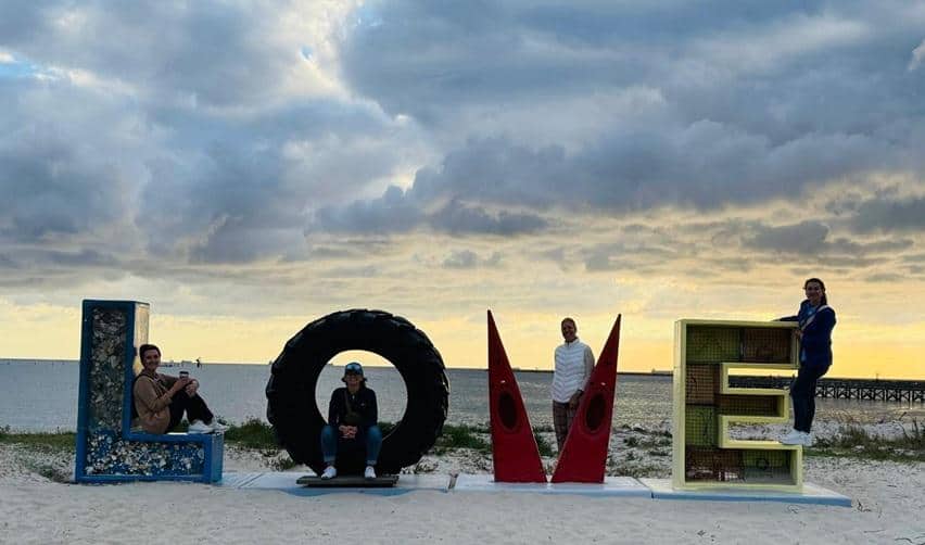 Bay Creek site visit guests posing playfully around the iconic LOVE sign on Cape Charles Beach at sunset, highlighting Virginia’s welcoming charm and coastal lifestyle.