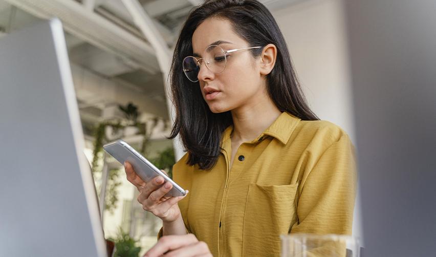 A professional woman checking her phone while working at a desk, representing an EB5 investor receiving automated USCIS case status updates through digital tracking tools.