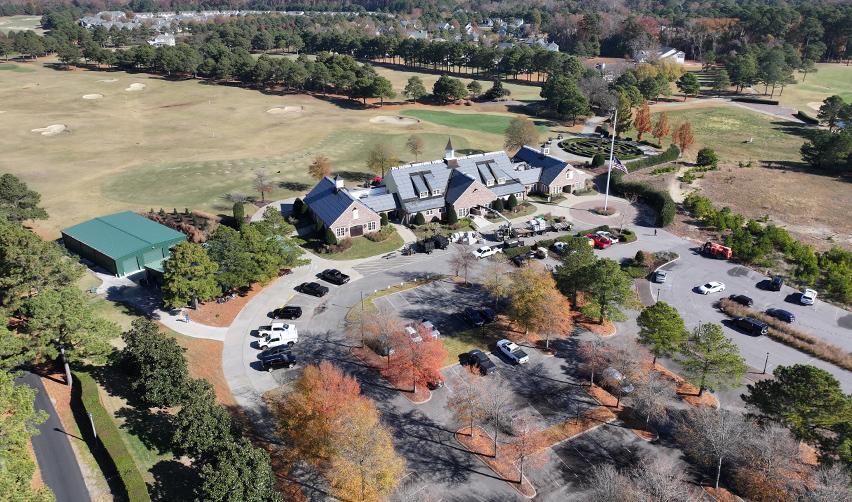 A wide aerial view of the Bay Creek Clubhouse surrounded by fall foliage, parking areas, and golf fairways as seasonal construction activity continues on the resort side.