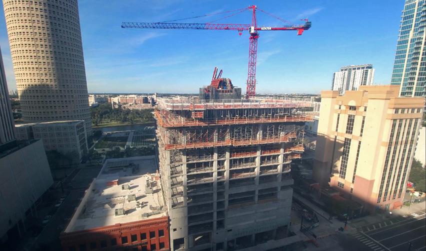 A downtown Tampa skyline view showing the ONE Tampa tower rising with multiple completed concrete levels and an active tower crane above, reflecting steady vertical construction progress for this EB5 project.