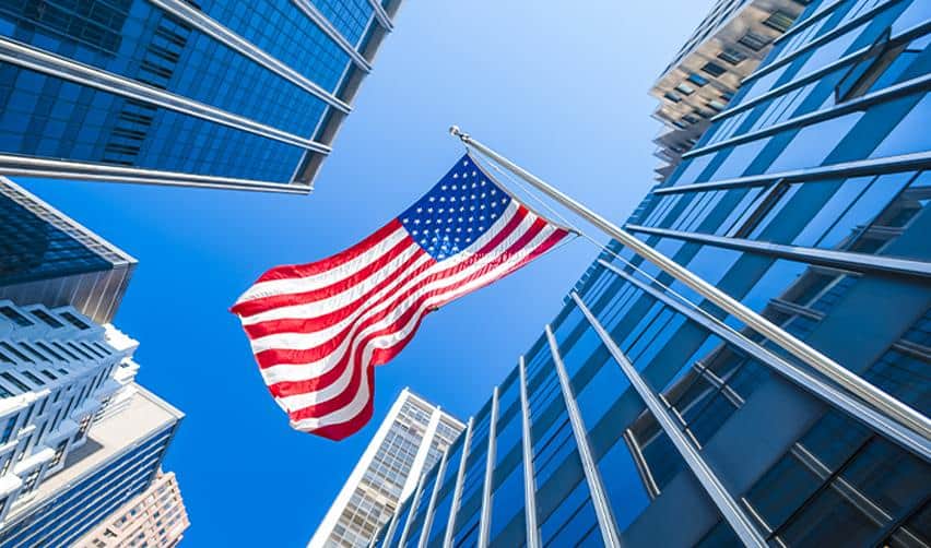 A US flag waving among tall city buildings, reflecting EB5 investment opportunities and business expansion in the United States.