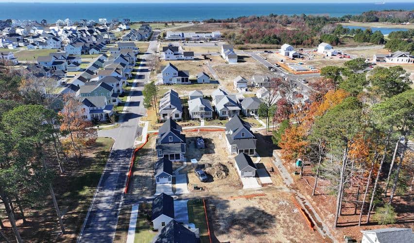 Aerial view overlooking a completed Bay Creek neighborhood beside ongoing Phase II construction, with coastal water views in the distance.