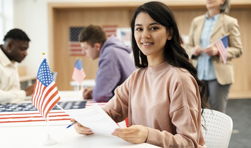 A female EB5 investor reviewing documents at a USCIS-style setting with U.S. flags, symbolizing the EB5 immigrant investor visa application process in 2026.