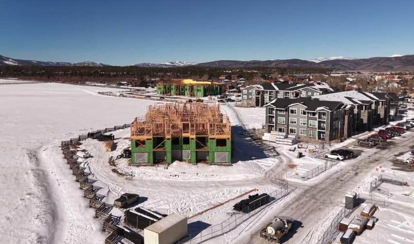 Aerial construction view of a multi-story building framed and sheathed at Grand Park, with nearby completed buildings and staging areas visible, illustrating active winter construction in the rural EB5 project.