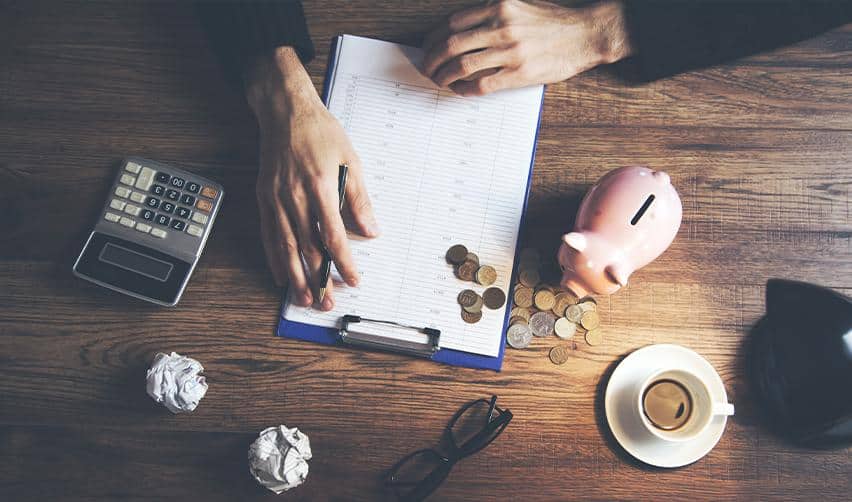 A top-down view of financial records, a calculator, and a piggy bank on a desk, representing EB5 investment planning, fund tracking, and sustainment of capital within an EB5 project.